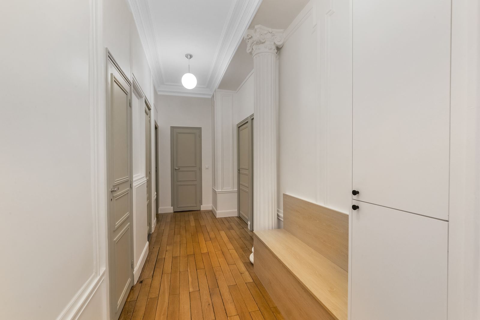 Couloir haussmannien d’un cabinet avec portes grises et parquet